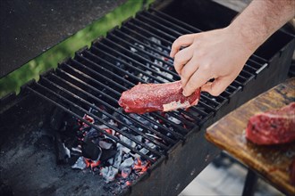 Unrecognizable man put raw strip steak on grill