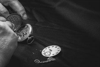 Opened pocket watch is repaired, dial and inner parts visible, on black fabric