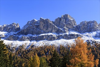 An impressive snow-covered mountain range above autumnal forests and rocks, Italy, Trentino-Alto