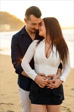 Vertical photo of a romantic couple embracing from the back on the beach during sunset