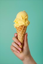 Hand holding yellow ice cream in cone in front of green studio background. KI generiert, generiert,