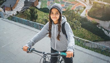 A smiling young girl with braids wearing a beanie descending urban stairs on her bicycle, AI