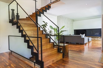 Black powder coated steel L-shaped staircase with stained and varnished wooden steps and tempered