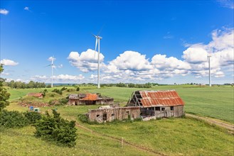 Old ruined farm in a rural landscape view with wind turbines on the fields in the summer, Sweden,