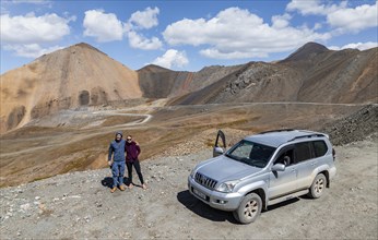 Two tourists with car at the mountain pass in Tien Shan, Chong Ashuu Pass, Kyrgyzstan, Issyk Kul,