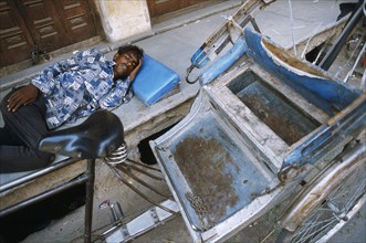 Man sleeping on the sidewalk. In the foreground, his rickshaw. Ajmer, Rajasthan, India, He is