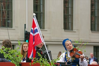 Woman in traditional traditional costume playing in the street, Norwegian national flag next to