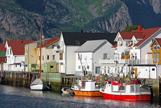 Fishing boats in front of wooden houses and high mountains in a small harbour, Idyll, Henningsvaer,