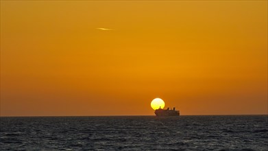The setting sun forms the backdrop for a ferry sailing on the sea in the distance, dusk, sunset,
