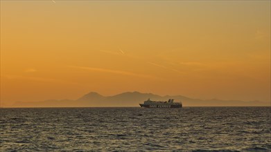 A ferry sails across the sea against a backdrop of an Orange coloured sunset, dusk, sunset, Western