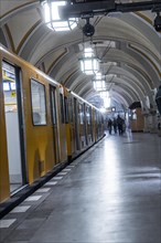 A yellow underground train stops at an arched platform underground, Heidelberger Platz, Berlin,