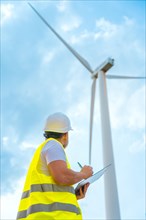 Vertical photo with low angle view of an engineer writing notes inspecting a wind turbine