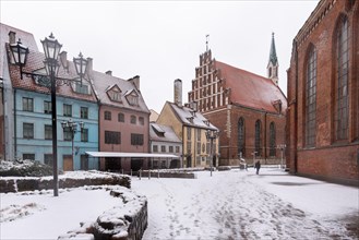 Snow-covered medieval houses stand in the street of butchers, Skarnu Iela, with St John's Church on