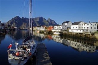 Sailing ships and wooden houses are reflected in the calm waters of a small harbour, Rorbuer,