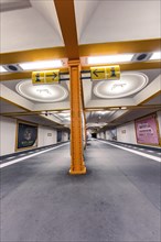 Underground station with artistic yellow columns and advertising posters on the walls, Berlin,