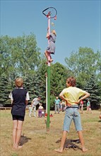 Girl climbing maypole, boys waiting, barefoot, Heiligenthal, Lower Saxony, Germany, 20/06/1992,