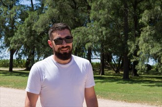 Man in white t-shirt, beard and sunglasses on farm smiling