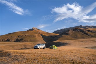 All-terrain vehicle Toyota Land Cruiser and green camping tent in the Kyrgyz highlands, hills with