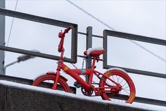Red children's bicycle in the snow, attached to a bridge railing, Riga, Latvia, Europe