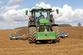 Green John Deere tractor ploughing deep furrows to prepare soil for potato crop, Ramsholt, Suffolk,