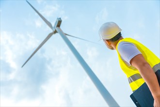 Low angle view photo of a male caucasian adult worker in protective gear looking up at a wind