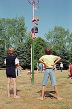 Girl climbing maypole, boys waiting, barefoot, Heiligenthal, Lower Saxony, Germany, 20/06/1992,