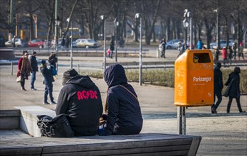 Young people sitting next to an orange-coloured waste bin of the Berlin city cleaning service,