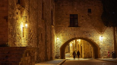 Night scene of a person walking under the arch of an illuminated building, night shot, Rhodes Old