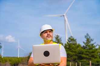 Engineer working using laptop standing in a park producing green energy with wind turbines