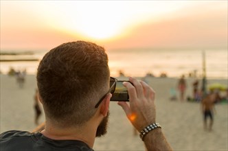 Man photographing sunset on the beach with smartphone