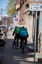 Two bicycle couriers with delivery backpacks ride on a city street, Riga, Latvia, Europe