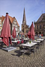 Outdoor area of a restaurant with red parasols and the Church of Our Lady on the market square in
