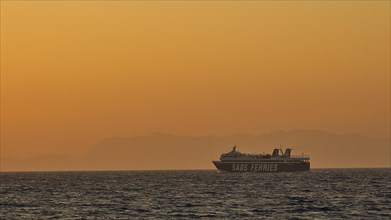 A ferry sails on the sea under a golden sunset sky, dusk, sunset, Western Promenade, Rhodes Town,