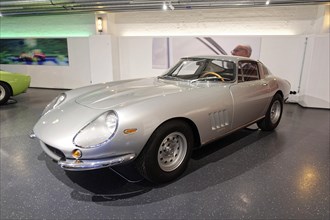 FERARI 275 GTB 4, A silver-coloured classic Ferrari in a showroom surrounded by other classic cars,