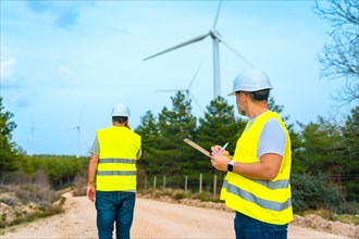 Technicians inspecting wind turbines in a green energy park talking to the mobile and taking notes