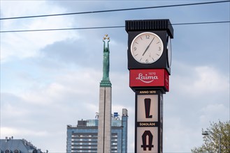 Laima clock, advertising traditional chocolate brand Laima, behind it the Freedom Monument with