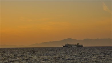 A ferry sails across the sea at sunset with an Orange coloured sky, dusk, sunset, Western