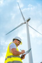 Vertical photo with low angle view of a smiling engineer writing notes inspecting a wind turbine in