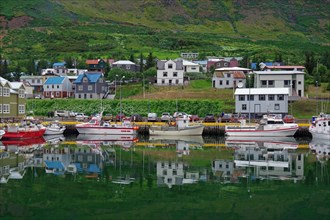 Fishing boats and houses reflected in the calm waters of a fjord, East Iceland, Seydisfjoerdur,