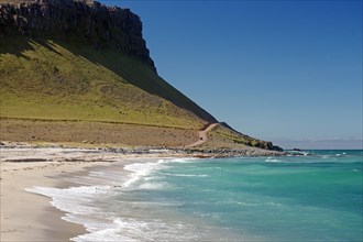 Lonely sandy beach and gravel track in front of vegetation-free mountains, Latrabjarg, Westfjords,