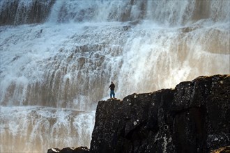 Man standing on a rock in front of the falling water of a waterfall, Dyandi, Westfjords, Iceland,