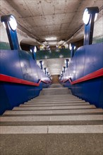 An empty staircase down to a Schloss Strasse underground station with characteristic blue colour