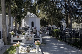 A white chapel surrounded by tombstones and an angel statue in a peaceful cemetery, Lindos, Rhodes,