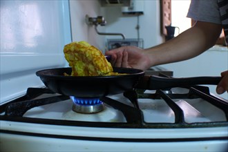 Person making a potato omelet in a frying pan on a butane stove