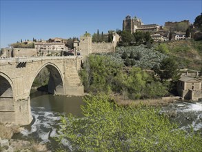 Stone bridge over the river, green hills with historical buildings and cathedral, clear blue sky,