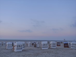 A quiet beach with white beach chairs and a gentle sunset in the sky, setting sun on a beach with