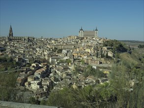 Historic city with river and numerous buildings, surrounded by hills, striking church towers, all