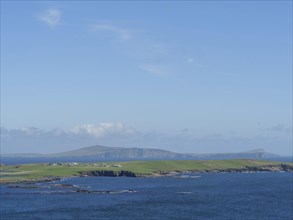 Vast coastal landscape with blue sky and green hills on the horizon, green meadows on a deep blue