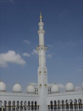 High tower of a mosque with white domes and golden accents under a clear sky, beautiful mosque with