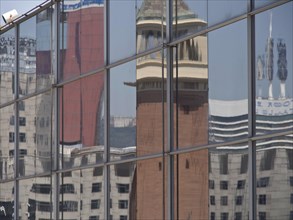 Reflection of a historic building in modern glass windows in an urban environment, two red towers